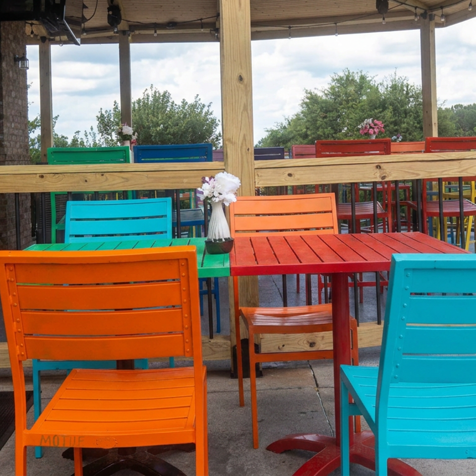Colorful orange, turquoise, green, and red patio tables and chairs on a covered restaurant deck overlooking trees.