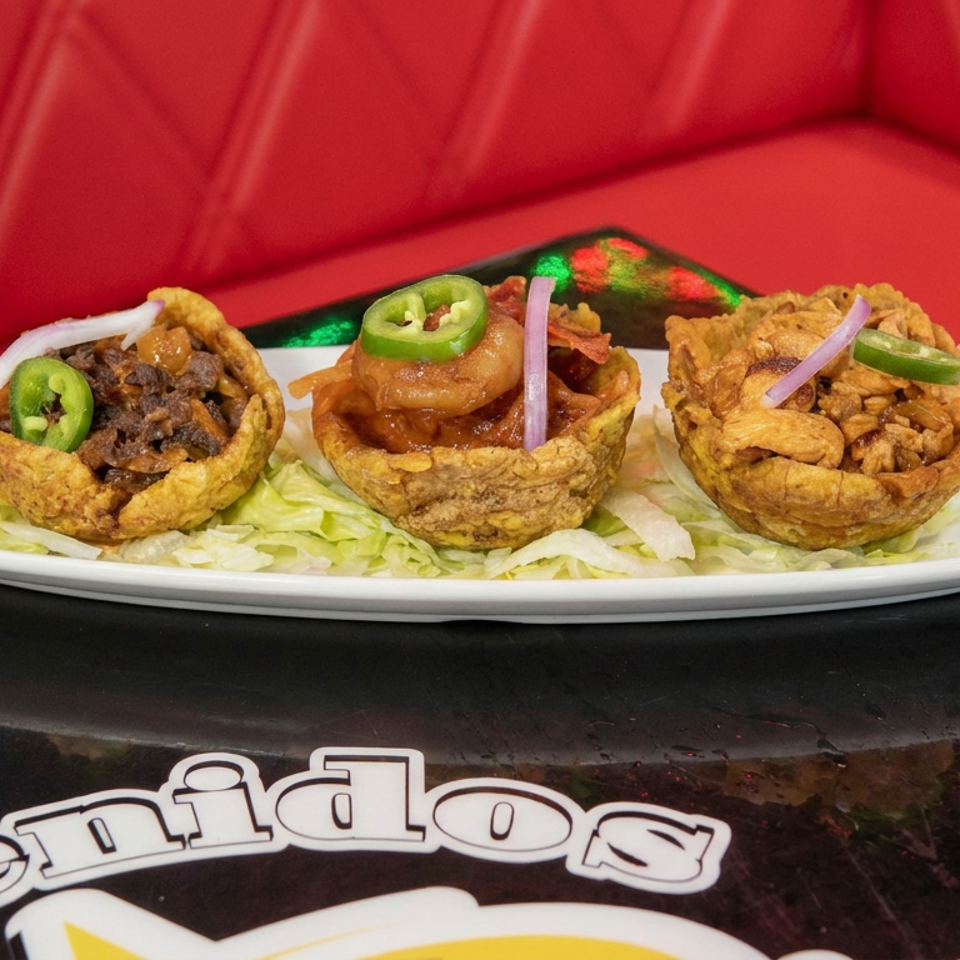 Three crispy fried plantain cups filled with savory toppings, garnished with jalapeño slices and red onion on shredded lettuce.